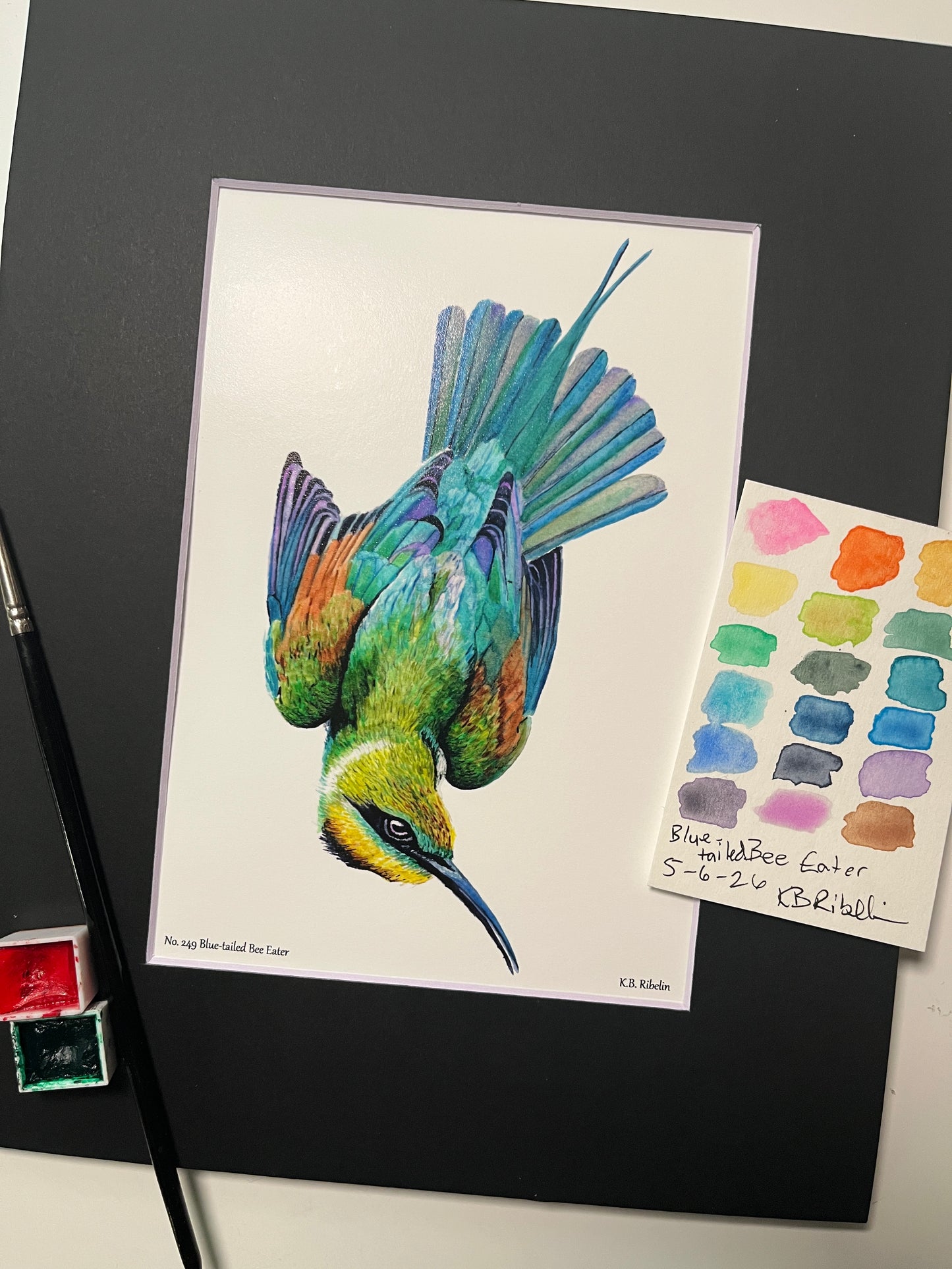 Giclee print of a painted bunting perched on a floral teacup displayed in a black mat.