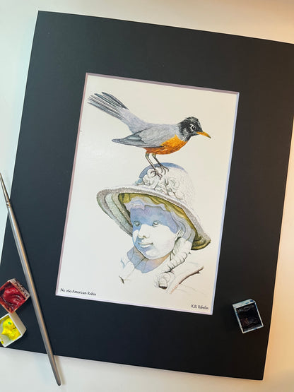Giclee print of a american robin perched on sculpted girl’s hat displayed in a black mat.