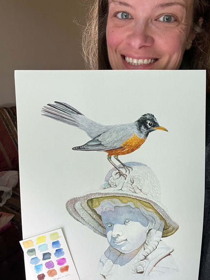 Artist holding the original painting of a american robin perched on sculpted girl’s hat, showing the artwork clearly.