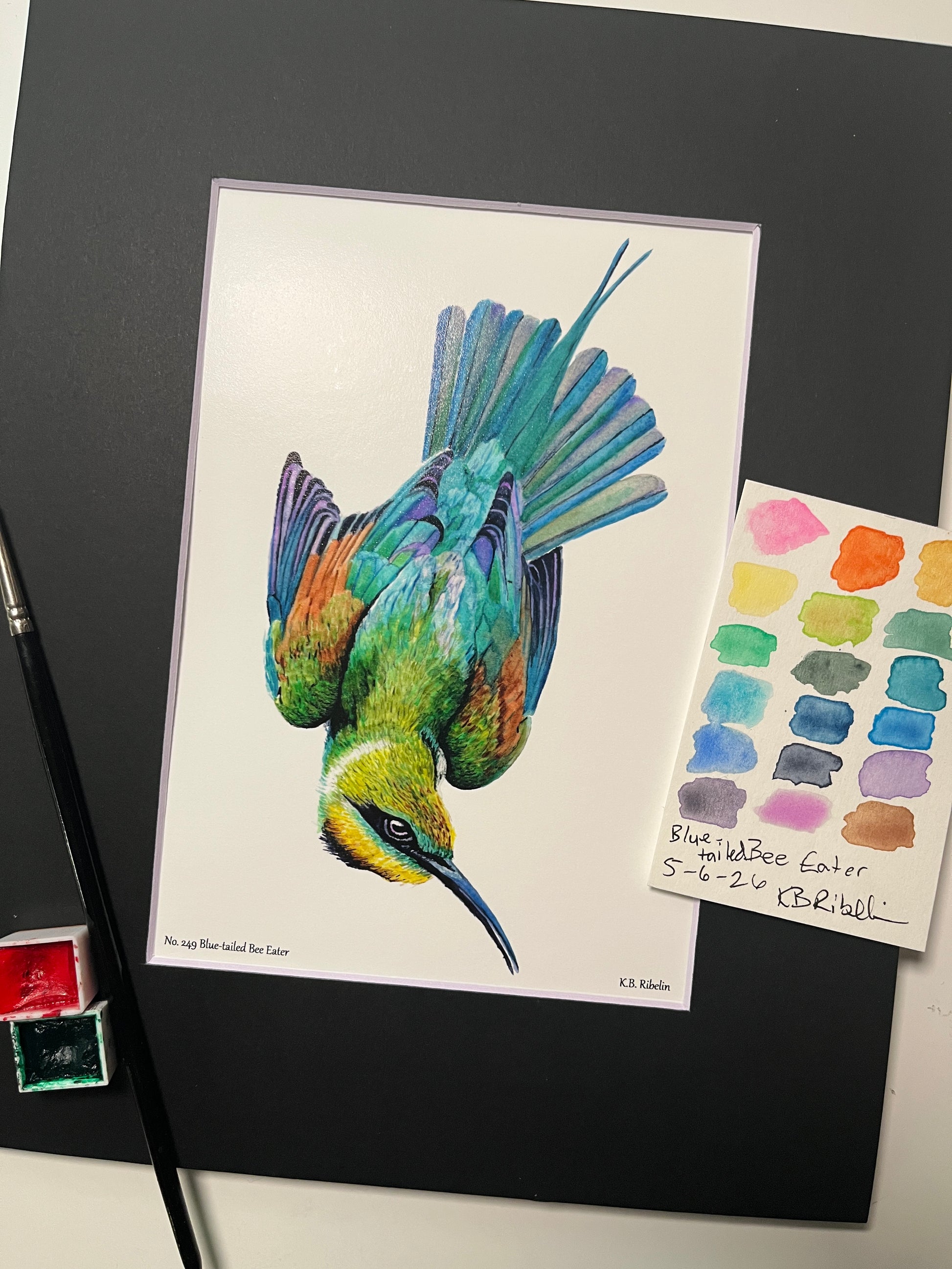 Giclee print of a painted bunting perched on a floral teacup displayed in a black mat.