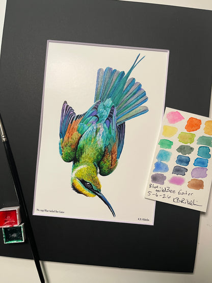 Giclee print of a painted bunting perched on a floral teacup displayed in a black mat.
