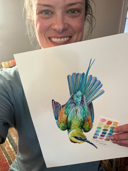Artist holding the original painting of a painted bunting perched on a floral teacup, showing the artwork clearly.
