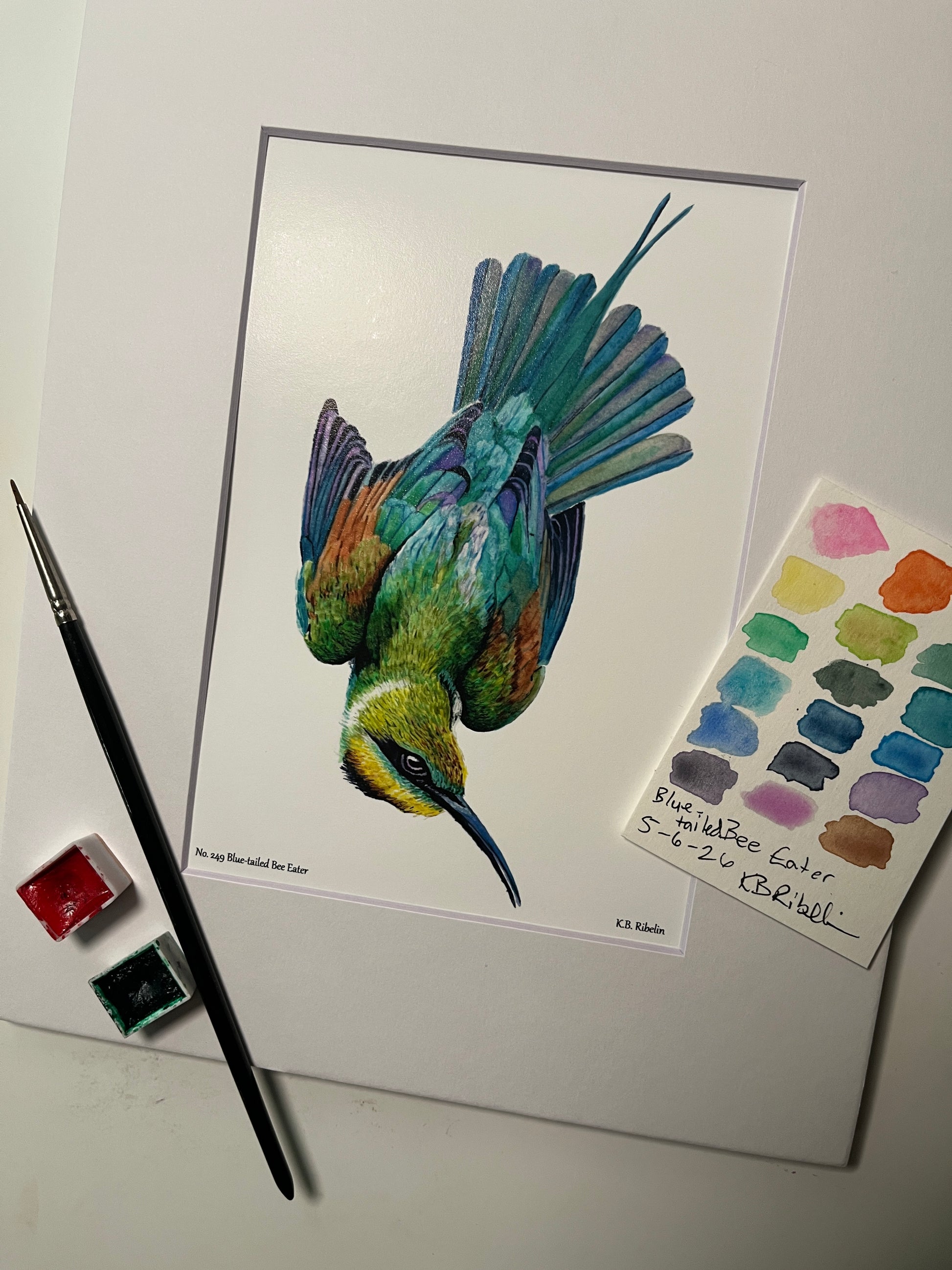 Giclee print of a painted bunting perched on a floral teacup displayed in a white mat.