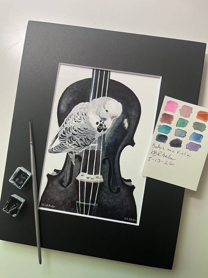 Giclee print of a soft blue‑green budgie perched on a violin watercolor displayed in a black mat.