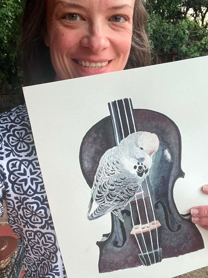 Artist holding the original painting of a soft blue‑green budgie perched on a violin watercolor, showing the artwork clearly.