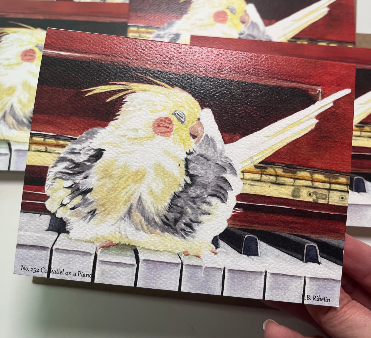 Single notecard printed with the cockatiel perched on a piano painting.