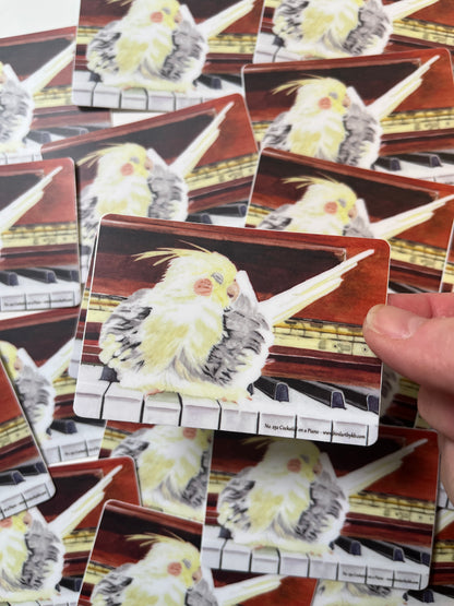 Sticker of the cockatiel perched on a piano artwork.