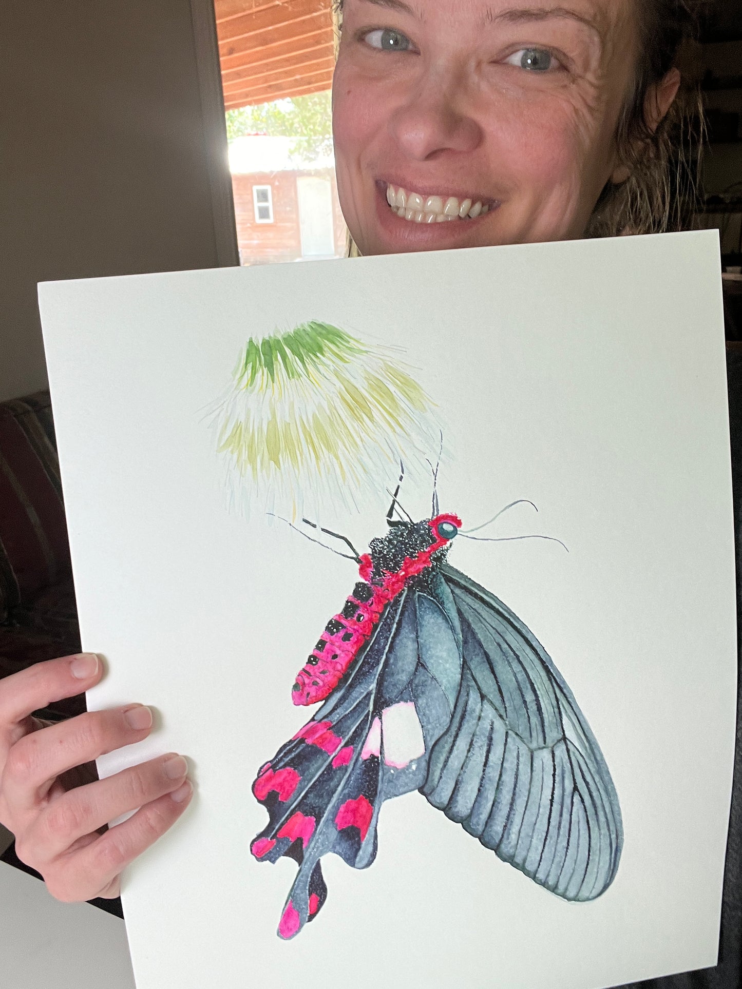 Artist holding the original painting of a common windmill butterfly with black wings and crimson markings watercolor, showing the artwork clearly.