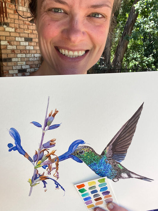 Artist holding the original painting of a fork‑tailed wood nymph hummingbird feeding from a tropical flower watercolor, showing the artwork clearly.