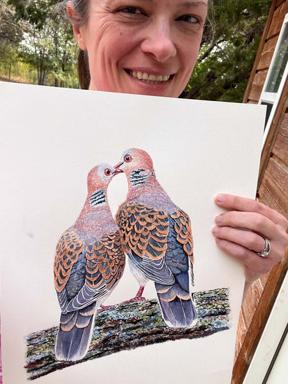 Artist holding the original painting of a two oriental turtle doves perched together touching beaks, showing the artwork clearly.