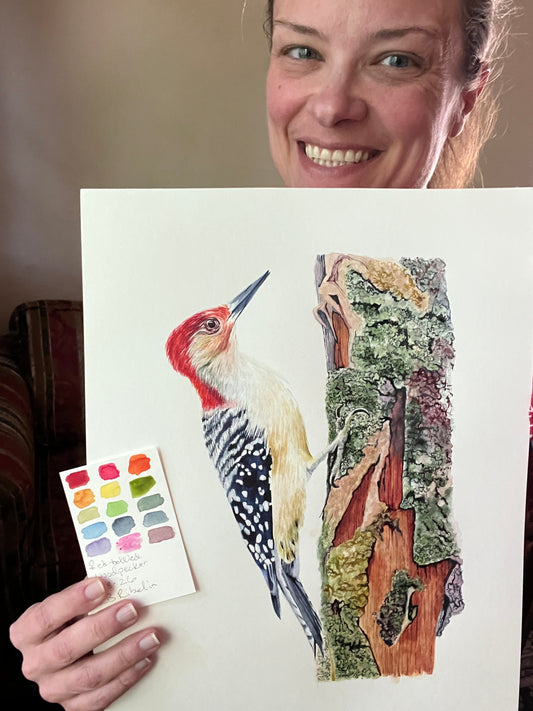 Artist holding the original painting of a red-bellied woodpecker perched on mossy tree bark with detailed forest textures, showing the artwork clearly.