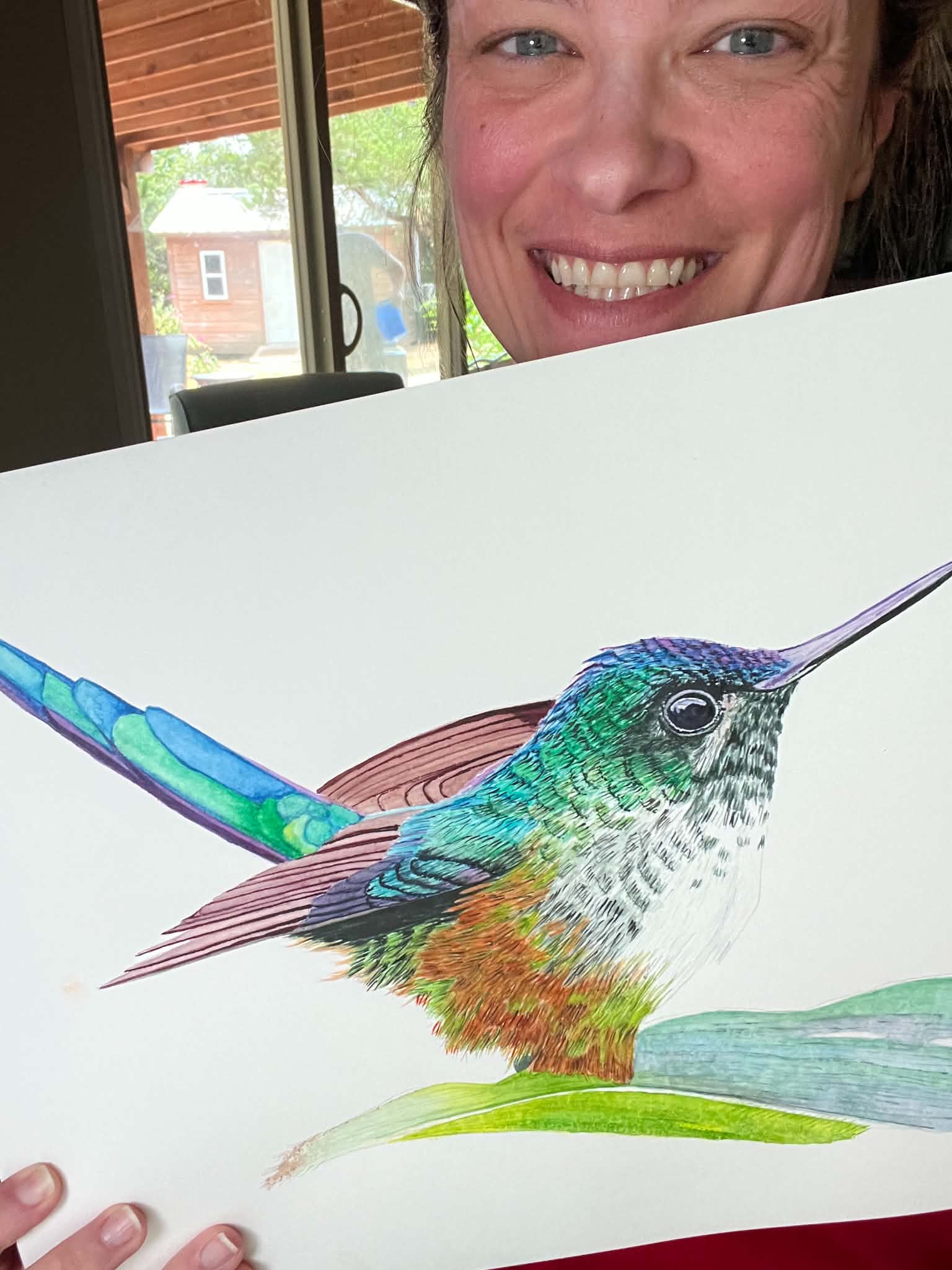 Artist holding the original painting of a violet‑tailed sylph hummingbird with emerald body and long violet tail streamers, showing the artwork clearly.