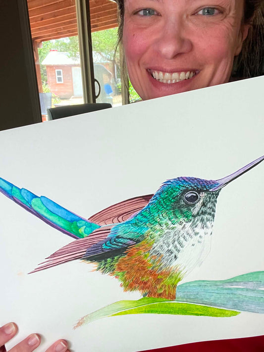 Artist holding the original painting of a violet‑tailed sylph hummingbird with emerald body and long violet tail streamers, showing the artwork clearly.