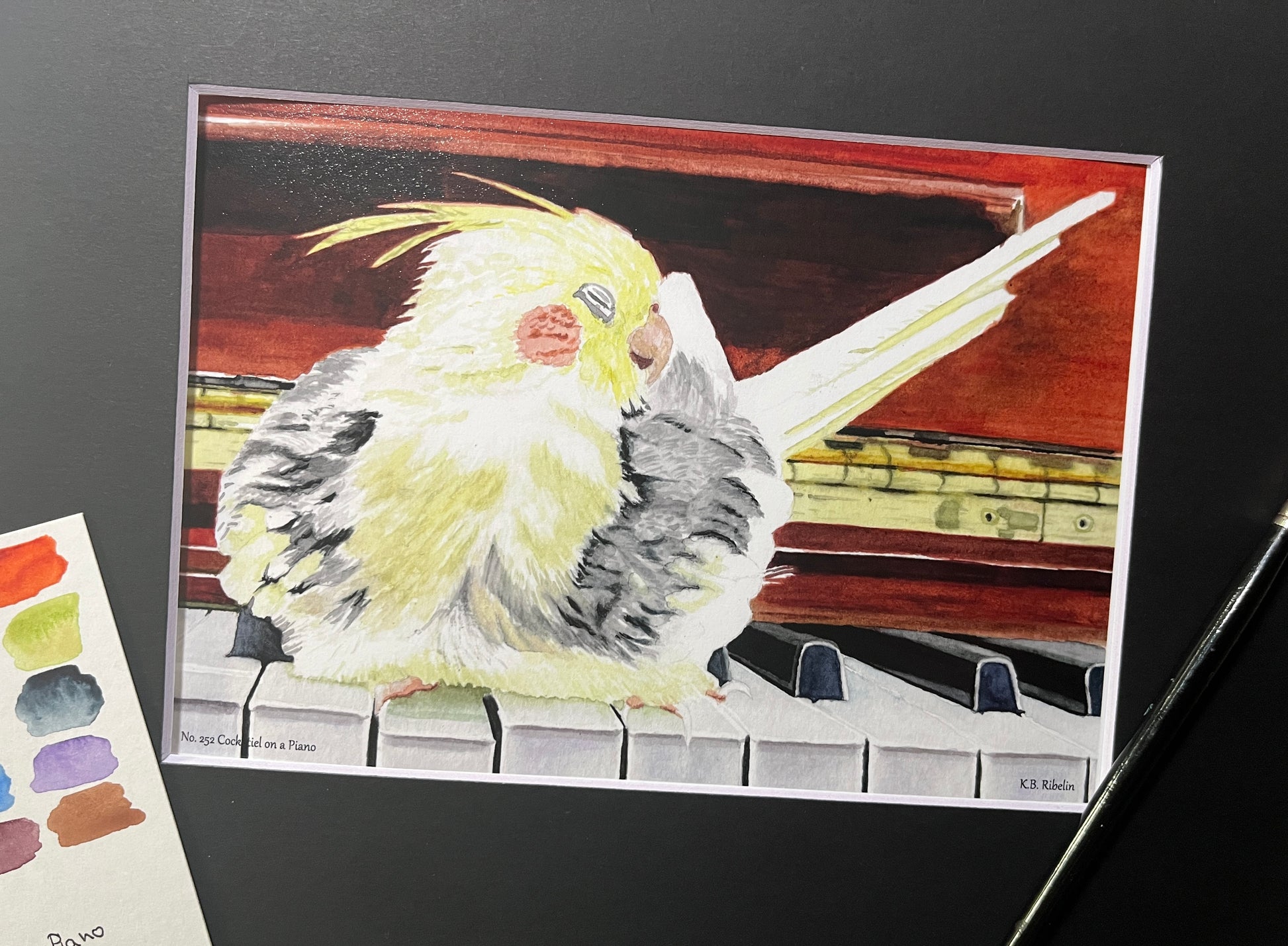 Giclee print of a cockatiel perched on a piano displayed in a black mat.