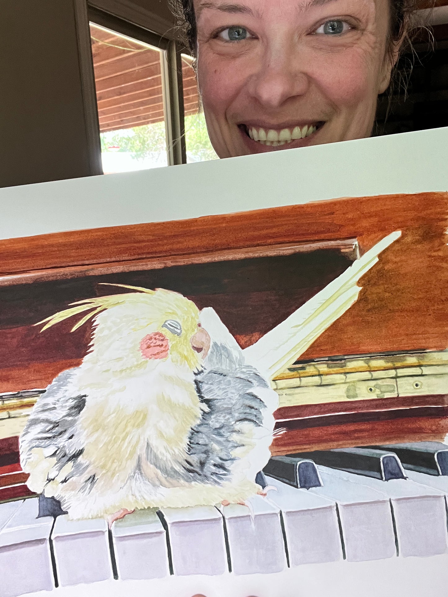 Artist holding the original painting of a cockatiel perched on a piano, showing the artwork clearly.