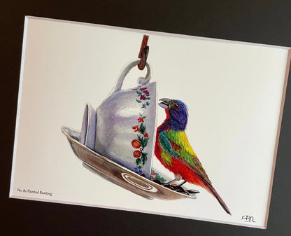 Giclée print of a painted bunting perched on a floral teacup displayed in a black mat.