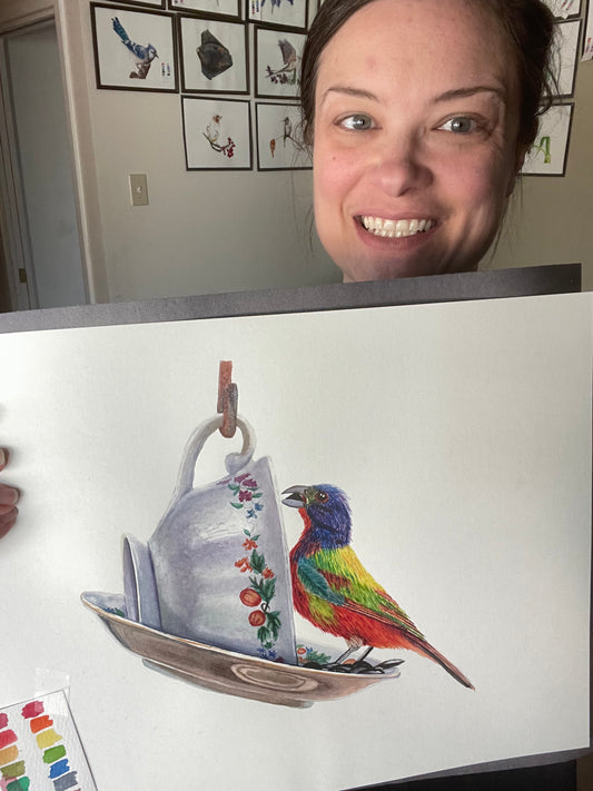 Artist holding the original painting of a painted bunting perched on a floral teacup, showing the artwork clearly.